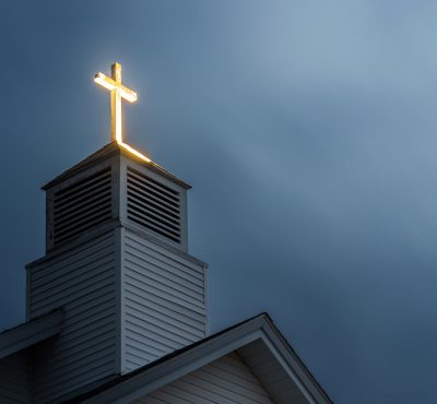 Image of church with lit cross and dramatic blue clouds in background.